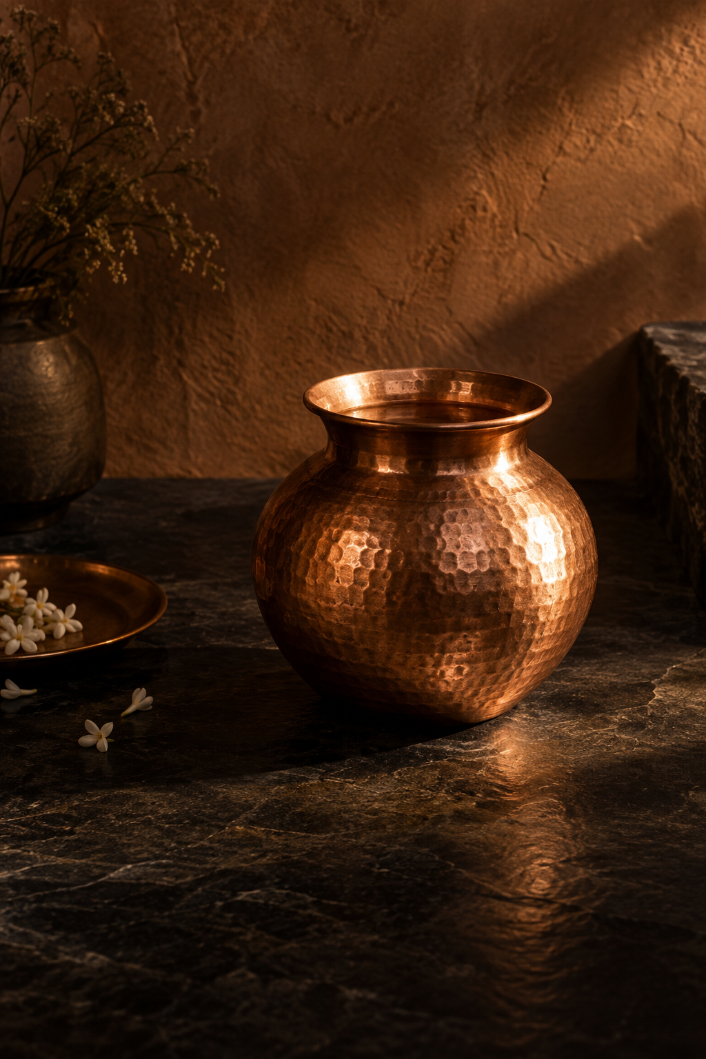 An unlabelled hammered copper vessel against a dark stone wall